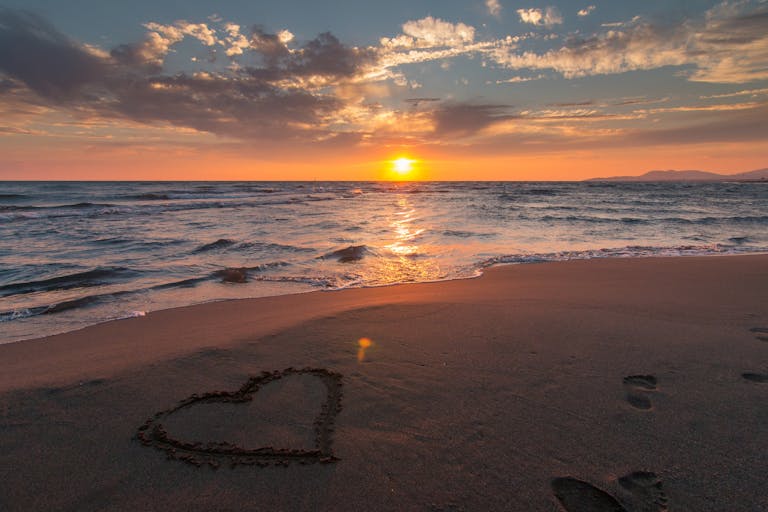 Beautiful sunset over ocean with a heart shape in the sand, perfect for romantic themes.